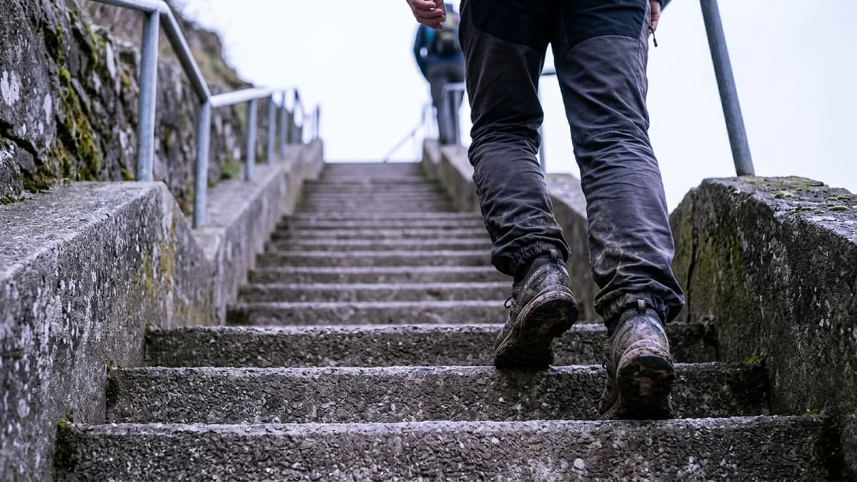 A person's legs climbing a steep outdoor concrete stairway under an overcast sky
