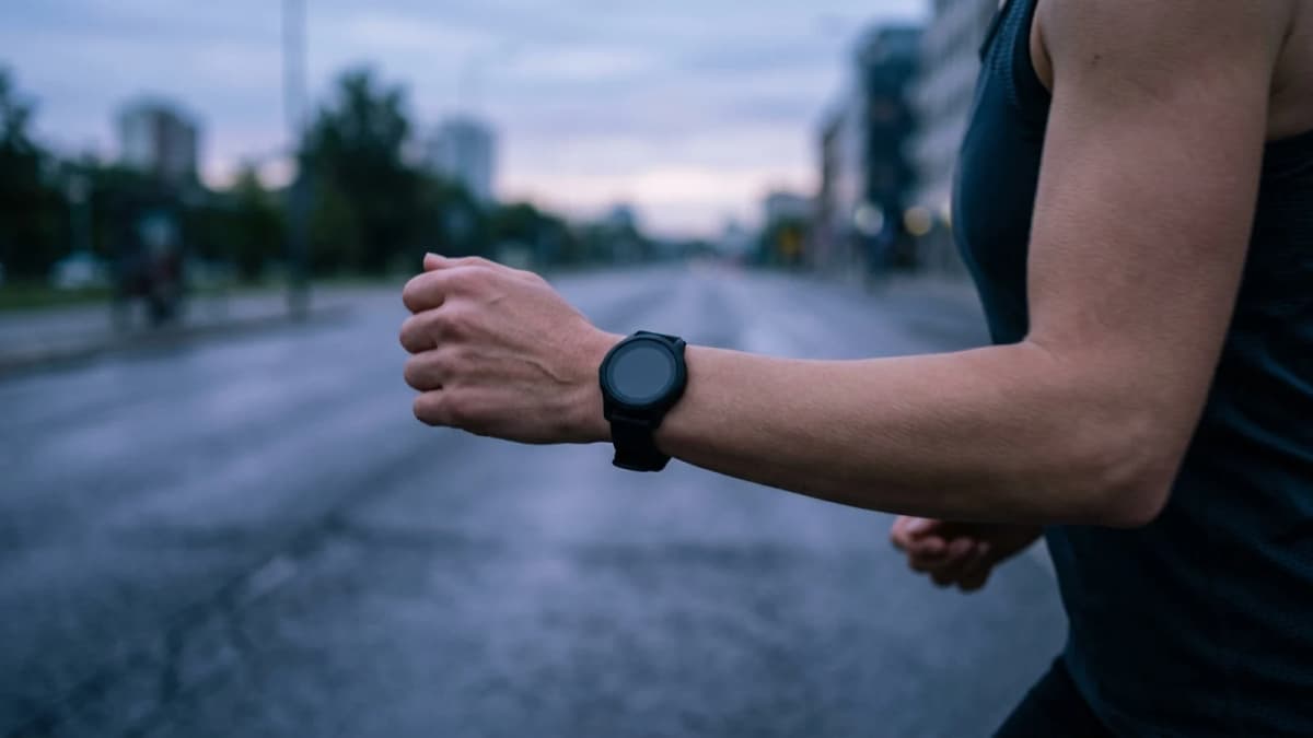 A runner's forearm with a plain wristband watch in motion on an empty street at first light