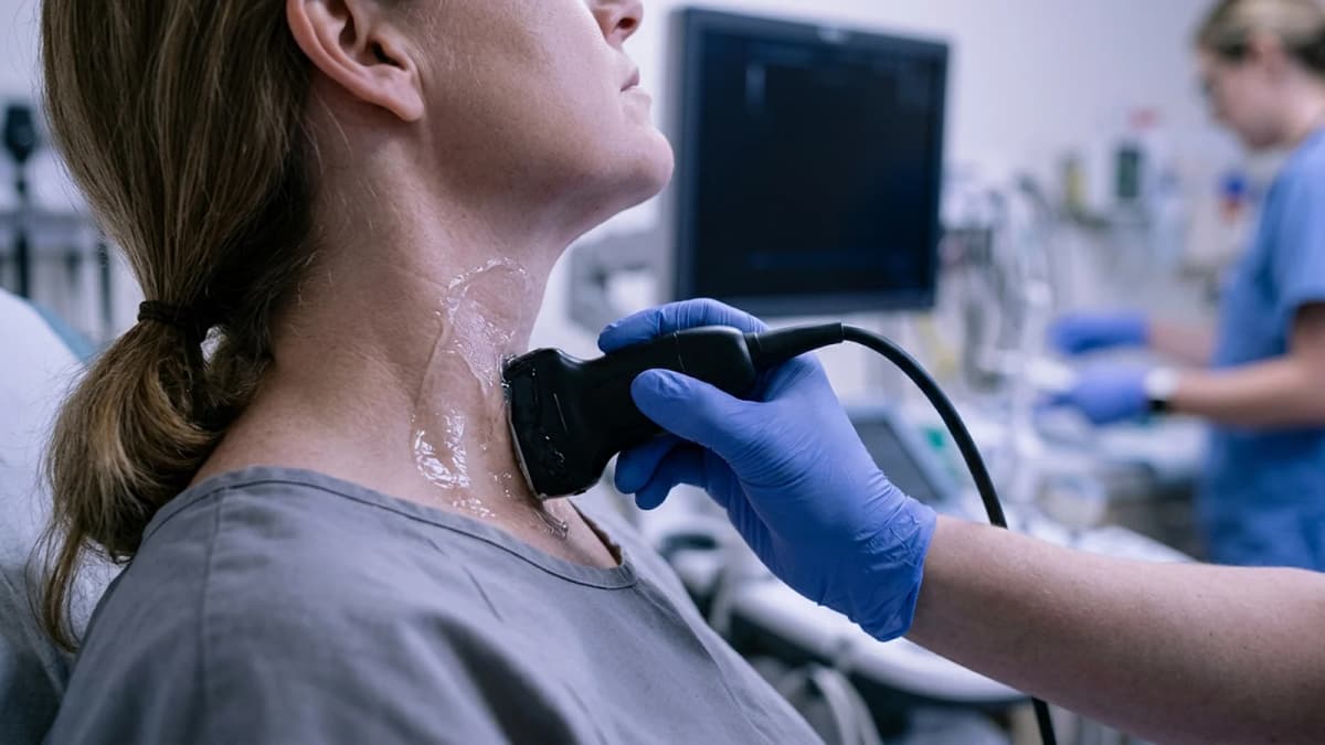 An ultrasound probe with gel pressed against the side of an adult neck during a thyroid scan