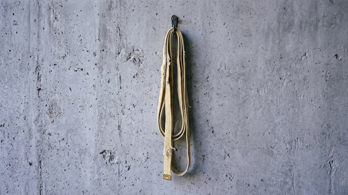 A cloth tape measure hanging from a hook against a plain concrete wall