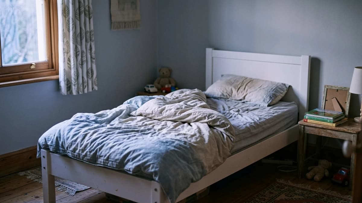 An empty child's bed with rumpled sheets in soft morning light