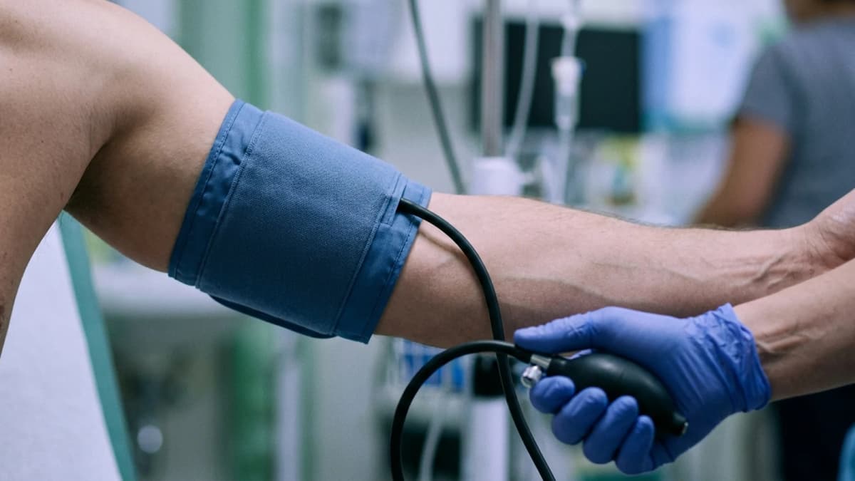 An inflating blood pressure cuff on an upper arm with a gloved hand on the bulb