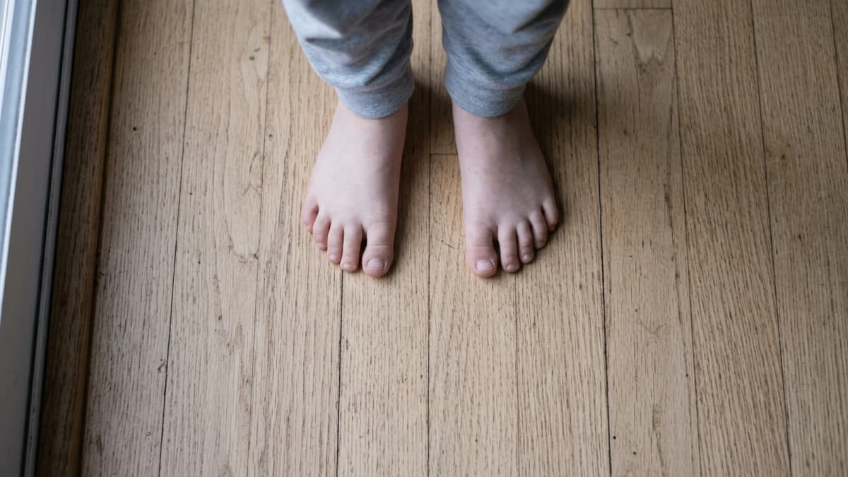 A child's bare feet standing flat on a wooden floor, seen from above