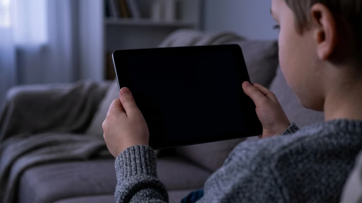 A child's hands holding a tablet with a blank screen in a dim room