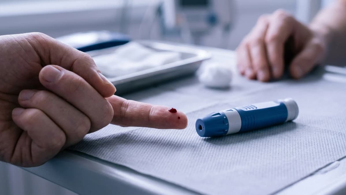 A fingertip with a single bead of blood beside a small lancing device