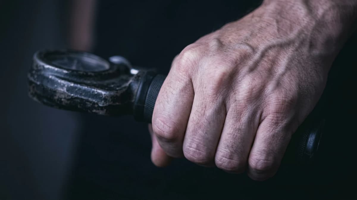 A hand squeezing a handheld grip dynamometer, shown close with the dial out of frame